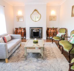 A living room with a gray sofa green upholstered chairs a glass coffee table and two wooden cabinets at Wisteria Cottage in Annagry County Donegal