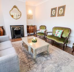 A living room with a gray sofa green upholstered chairs a coffee table fireplace and a patterned rug at Wisteria Cottage in Annagry County Donegal