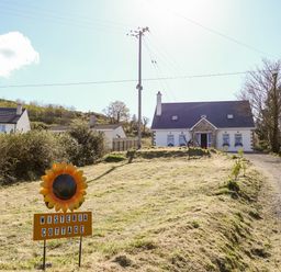 A house with a stone driveway and a sign reading Wisteria Cottage in the front yard at Wisteria Cottage in Annagry County Donegal