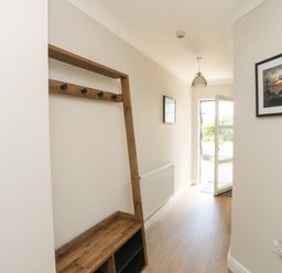 A hallway with a wooden coat rack bench light fixture open door and framed pictures at 4 Pen Llanw Tides Reach in Rhosneigr