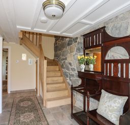 A hallway with wooden stairs a vintage wooden hall stand with a cushion and vases with flowers on a stone wall at Bryn Moelyn Cottage in Yr Efail near Morfa Nefyn