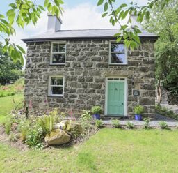 A stone cottage with a green door and flower beds in front at Bryn Moelyn Cottage in Yr Efail near Morfa Nefyn