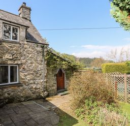 A stone exterior cottage with two windows and a wooden door near a garden and lattice fence at Gilfachwydd in Islawrdref near Dolgellau