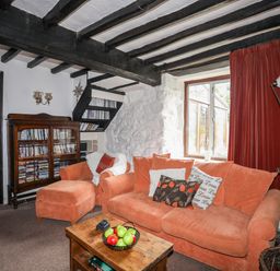 A living room with orange sofas a wooden coffee table a bookshelf and a window with red curtains at Gilfachwydd in Islawrdref near Dolgellau