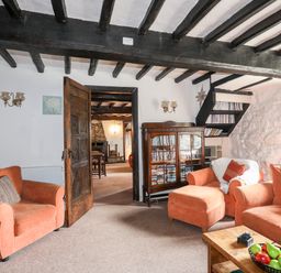 A sitting room with orange armchairs and sofa wooden cabinet and exposed wooden ceiling beams at Gilfachwydd Islawrdref near Dolgellau