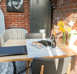 A table with chairs near a brick wall with flowers a bottle of champagne and muffins at Farriers Retreat in Budleigh Salterton