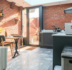 A kitchen with a table and chairs near a glass door and brick walls at Farriers Retreat in Budleigh Salterton