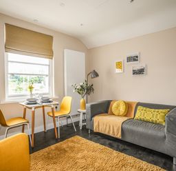 A living room with a grey sofa a yellow rug and a small dining table with two yellow chairs at Cwm Gwyrfai in Caernarfon