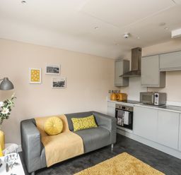 A kitchen and living area with a grey sofa yellow cushions yellow toaster microwave oven and a small dining table at Cwm Gwyrfai in Caernarfon