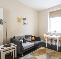 A living room with a gray sofa yellow chairs a white dining table a floor lamp and a small plant on tables at Moel Tryfan in Caernarfon