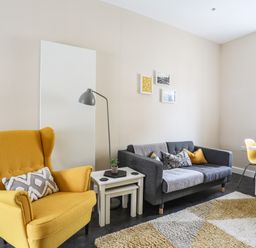 A living room with a yellow armchair a gray sofa with cushions white nesting tables and a dining table at Moel Tryfan in Caernarfon