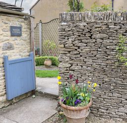 A stone wall with a blue wooden gate and a planter with flowers at Manor Cottage in Poulton