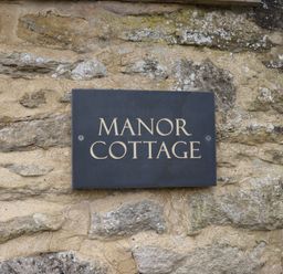 A stone wall with a sign reading Manor Cottage at Manor Cottage in Poulton