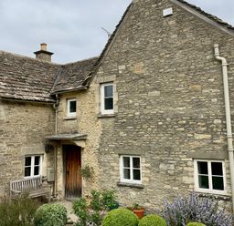 An exterior view of a stone house with wooden door white framed windows garden bench and plants in front at Manor Cottage in Poulton