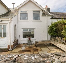 An outdoor patio area with stone paving a wooden bench and shrubs at 1 Salt Cottage in Port Eynon