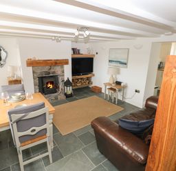 A living room with a fireplace a dining table a leather sofa and stairs at 1 Salt Cottage in Port Eynon
