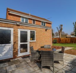 A brick house with two white doors and a small window overlooking a patio with a round table and four chairs at Robellen Corner in Adderbury