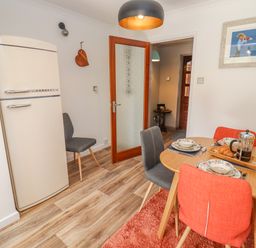 A dining area with wooden table set for breakfast with orange and gray chairs a cream refrigerator and a wooden door at Robellen Corner in Adderbury