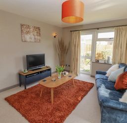 A living room with a blue sofa orange pillows a wooden coffee table a TV on a stand and a red rug at Robellen Corner in Adderbury
