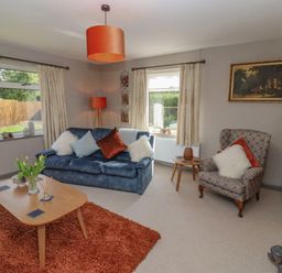 A living room with a blue sofa and orange rug at Robellen Corner in Adderbury