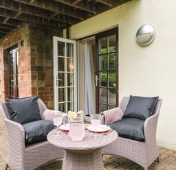 A patio with two cushioned chairs and a round table with a pitcher and glasses outside a building with open French doors at Cosy Corner in the Lakes in Greystoke