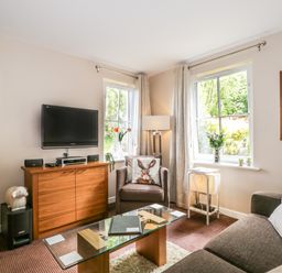 A living room with a brown sofa, armchair, glass coffee table, wooden cabinet with TV and two windows at Cosy Corner in the Lakes in Greystoke