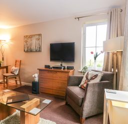 A living room with a glass coffee table a brown armchair and a wooden cabinet with a TV on it at Cosy Corner in the Lakes in Greystoke