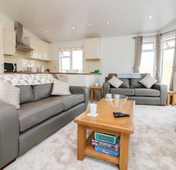 A living room with two gray sofas a wooden coffee table with board games and a kitchen area at Ridge's Retreat No 7 Kigbeare Lodges Ashbury Resort near Fowley Cross Sourton Down and Okehampton