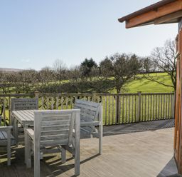 A wooden deck with table and chairs overlooking green fields and trees at Ridges Retreat No 7 Kigbeare Lodges Ashbury Resort near Fowley Cross Sourton Down and Okehampton