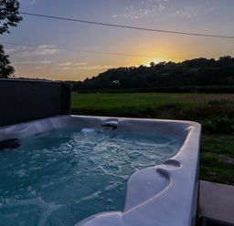 An outdoor hot tub with bubbling water overlooking a field and hills at sunset at Plas Glan Yr Afon in Llangernyw