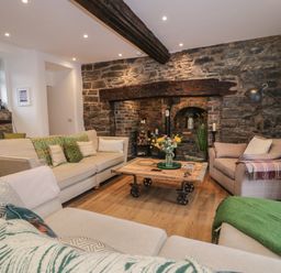 A living room with beige sofas and a wooden coffee table in front of a stone wall fireplace at Plas Glan Yr Afon in Llangernyw