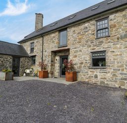 Stone house with slate roof and chimney with gravel driveway and potted plants at Plas Glan Yr Afon in Llangernyw