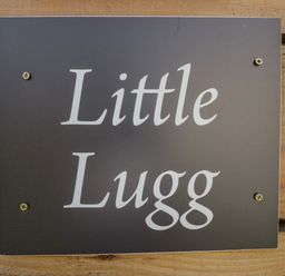 A black sign with white text reading Little Lugg mounted on a wooden surface at Little Lugg in Cross Keys near Hereford