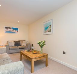 A living room with two sofas a wooden coffee table with flowers and snacks and framed pictures on the walls at Golden Sands in Carbis Bay