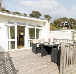 A wooden deck with outdoor dining table and chairs outside a white house with large windows at Seas The Day in Ventnor