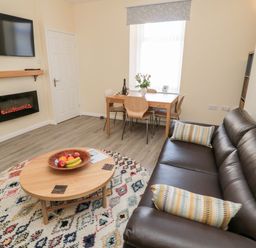A living room with a brown leather sofa a round rug and a wooden coffee table at Stones Throw in Amble