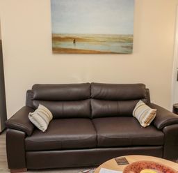 A brown leather sofa with two striped cushions a wooden side table a shelving unit and a painting on the wall at Stone's Throw in Amble