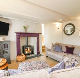 A living room with a lit fireplace a television on the wall sofas with floral and plain cushions and a round mirror on the wall at Hillside in Crafthole