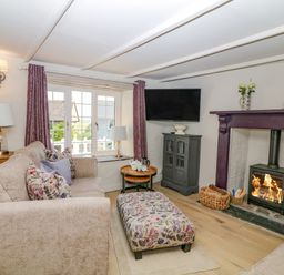 A living room with sofas a floral ottoman a wood burning stove and a wall mounted TV at Hillside in Crafthole