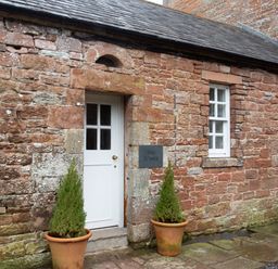 A stone building exterior with a white door two potted plants and two windows at The Tower in Kirklinton near Longtown
