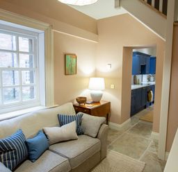 A living room with a gray sofa and blue cushions next to a window and a side table with a lamp and a wooden bowl at The Tower in Kirklinton near Longtown