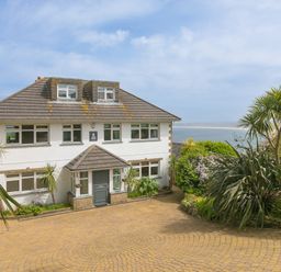 A two story house with multiple windows a gray roof and a paved driveway with plants and trees near the house at Moonbeams in Carbis Bay