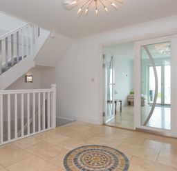 An entryway with tiled floor and circular mosaic design staircase with striped carpet and glass double doors leading to another room at Moonbeams in Carbis Bay