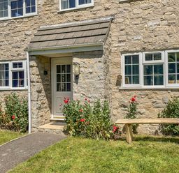 Stone house front with a small porch door red flowers near windows and a wooden bench at West Lulworth Apartment in West Lulworth