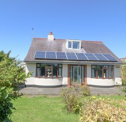 A house with solar panels on the roof and a green garden in front at Awelfryn in Elim near Llanddeusant