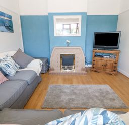 A living room with a fireplace a television on a wooden cabinet and grey sofas at Awelfryn in Elim near Llanddeusant