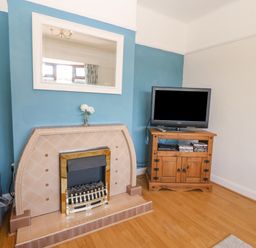 A living room with a tiled fireplace a wall mirror a small wooden cabinet with a television and a vase with flowers at Awelfryn in Elim near Llanddeusant