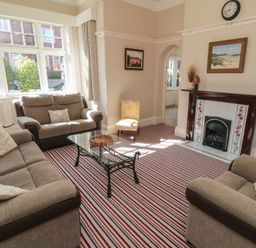 A living room with sofas glass coffee table striped carpet and fireplace at Lonsdale Villa in Scarborough