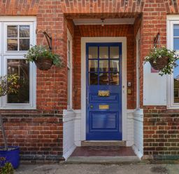 A blue front door with a welcome sign framed by red brick walls and windows with hanging flower baskets at Lonsdale Villa in Scarborough