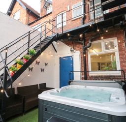 An outdoor area with a hot tub seating under stairs with potted plants and string lights at Lonsdale Villa Scarborough